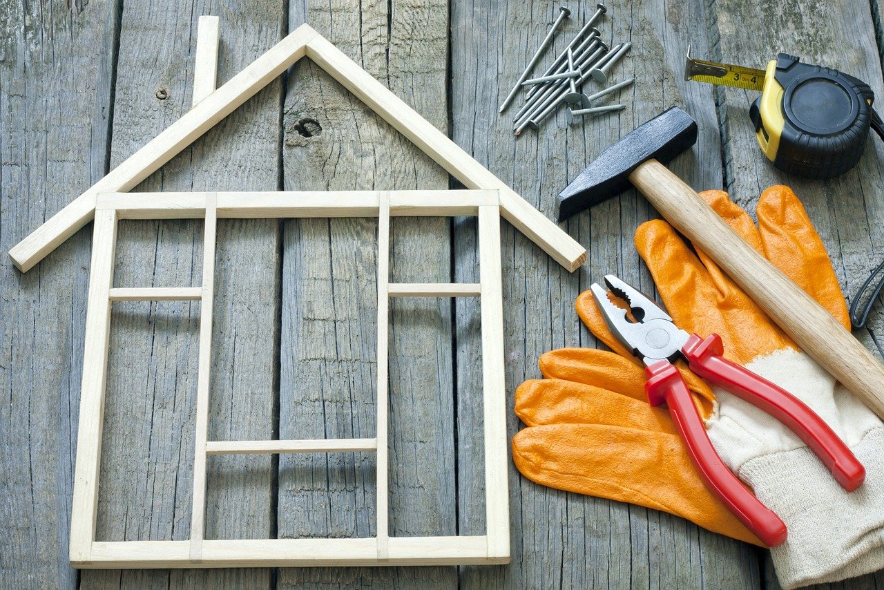 DIY home improvement tools and a wooden house outline on a table, representing property upgrades and energy-efficiency improvements.